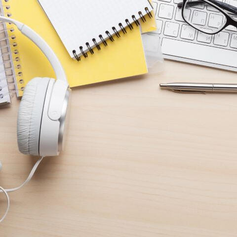 Tools for writing, like a notebook, pen, laptop, glasses, and headphones